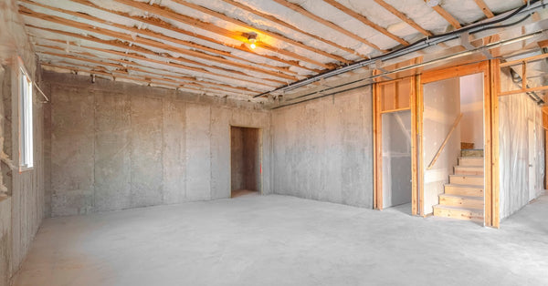 The concrete basement of a new build home under construction features a tall ceiling and wooden stairs.