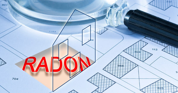 A magnifying glass sits atop a large home blueprint, and the word "radon" in red is in the home's basement.